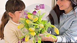 A little girl gives a bouquet of yellow and purple tulips to her mother. Affectionate loving hugs of daughter and mom on