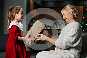 Little girl giving a big wrapped present box to her grandma for christmas