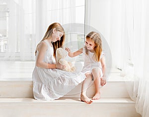 Little girl giving her teddy bear toy to older sister