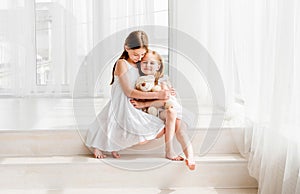 Little girl giving her teddy bear toy to older sister