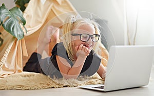 Little girl with glasses having fun with laptop on the floor in her room