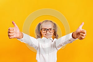 Little girl in glasses shows thumb up with two hands.