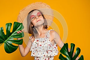 little girl in glasses and a straw hat on a yellow background in the studio