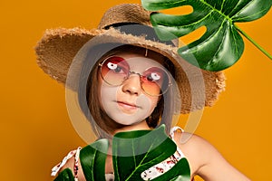 little girl in glasses and a straw hat on a yellow background in the studio