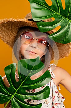 little girl in glasses and a straw hat on a yellow background in the studio