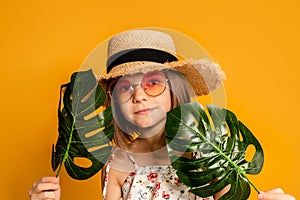 little girl in glasses and a straw hat on a yellow background in the studio