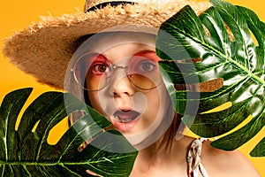 little girl in glasses and a straw hat on a yellow background in the studio