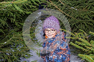 Little girl in glasses in winter among fir trees