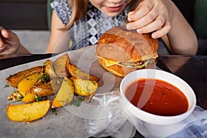 a little girl with gloves eats a burger and potatoes in a summer outdoor cafe.