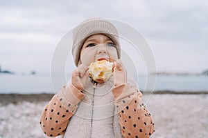 Little girl gnaws a big apple while holding it in her hands on the seashore