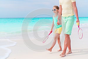 Little girl going to play tennis with father on white tropical beach