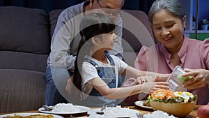 Little girl granddaughter enjoying to eat food with grandparents