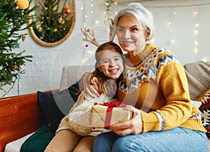 Little girl granddaughter giving Christmas gift box to smiling grandmother during winter holidays