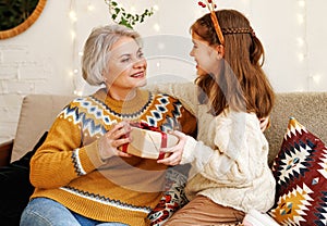 Little girl granddaughter giving Christmas gift box to smiling grandmother during winter holidays