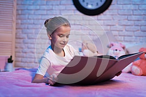 Little girl, granddaughter is reading book at night at home.