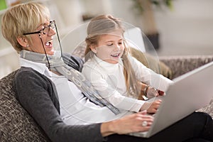 Little girl and granny together using laptop at home