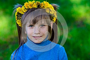 Little girl on a green grass in a wreath of flowers in spring