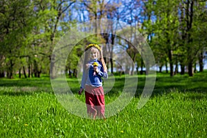 Little girl on a green grass in a wreath of flowers in spring