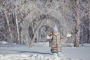 Little girl in grey jacket plays with snow in winter forest