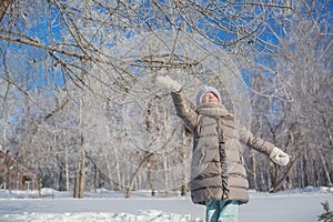 Little girl in grey jacket plays in winter forest in sunny day