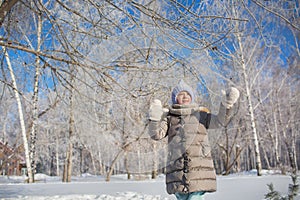 Little girl in grey jacket walks in winter park in sunny day