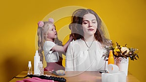 A little girl hairdresser dries her client's hair on a yellow background. Children as adults