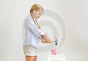 Little girl with hammer by the pink pig piggy bank