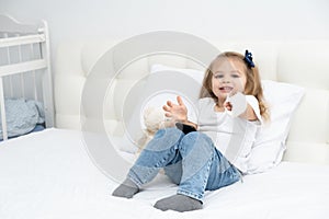 Little girl with hand in plaster sitting in bed showing the class, using smartphone