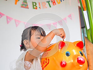 The little girl hand putting coin in the golden piggy bank received at a birthday party