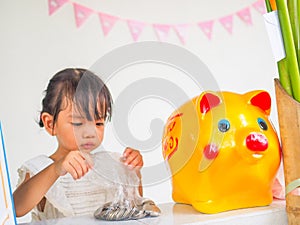 The little girl hand try to putting coin in the golden piggy bank received at a birthday party