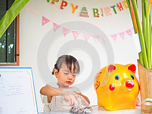 The little girl hand try to putting coin in the golden piggy bank received at a birthday party