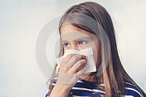 Little girl with handkerchief. A cold girl blows her nose in a white rag on a blue background. Diseases and colds. Rhinitis snot