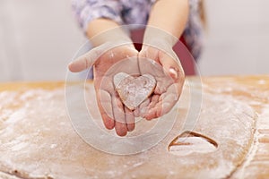 Little girl hands with cookie in the sahep of a heart cut from the stretched dough