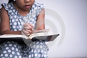 Little girl hands folded in prayer on a Holy Bible