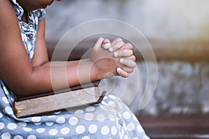 Little girl hands folded in prayer on a Holy Bible