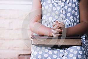 Little girl hands folded in prayer on a Holy Bible