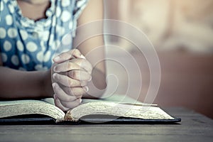 Little girl hands folded in prayer on a Holy Bible