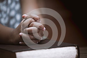 Little girl hands folded in prayer on a Holy Bible in church