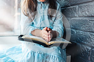 Little girl hands folded in prayer on a Holy Bible in church for faith concept in vintage color tone