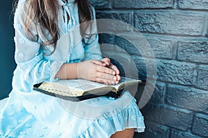 Little girl hands folded in prayer on a Holy Bible in church for faith concept in vintage color tone