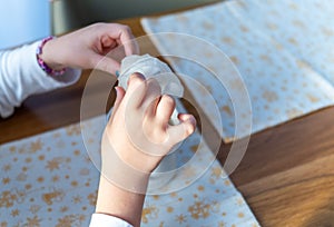 little girl hands with a tissue over a table, indoor closeup