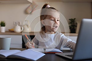 Little girl handwrite study online using laptop at home, cute happy small child take Internet web lesson or class on PC