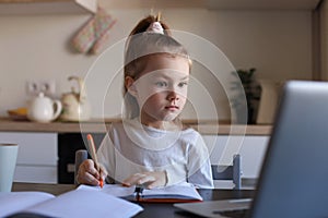 Little girl handwrite study online using laptop at home, cute happy small child take Internet web lesson or class on PC photo
