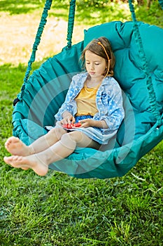 A little girl the on hanging chair outdoors play pop it, kid hands playing with colorful pop It
