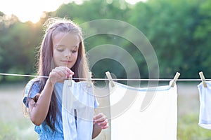 Little girl hangs out to dry retro doll clothes, summer nature outdoor. Washing, children`s games, kid`s leisure