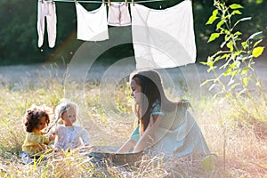 Little girl hangs out to dry retro doll clothes, summer nature outdoor. Washing, children`s games, vintage style