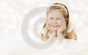 Little girl happy smiling, lying down hands under cheeks. White