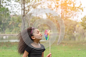 Little girl happy smiling and playing outdoor. Lovely girl  blowing small windmill in the park