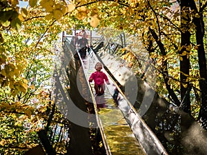 Little girl has fun on a very long steel slide that passes through the branches of the trees