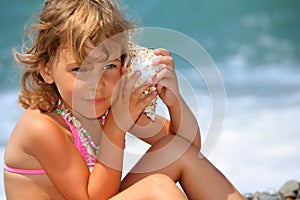 Little girl has leant seashell bowl to an ear